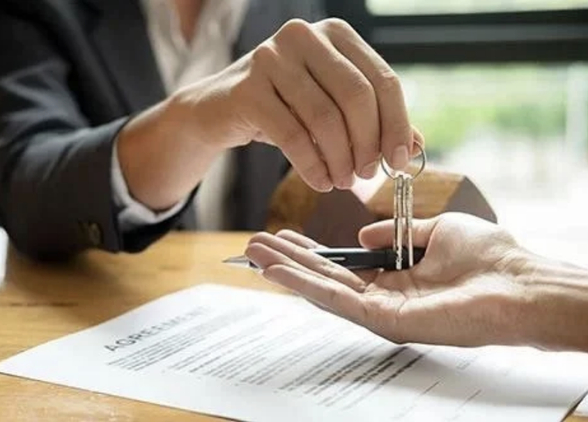 A close-up image of a person in a suit handing over keys to another person, with a document on the desk labelled ‘Agreement’, symbolising property settlements in family law.